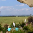 Flugplatz Paderborn-Haxterberg (Terrasse) Blick von einer Terrasse auf eine weite Wiesenlandschaft mit Menschen und Sonnenschirmen.