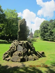 Großer, markanter Stein im Vordergrund, mit Hermannsdenkmal im Hintergrund, umgeben von Wald.
