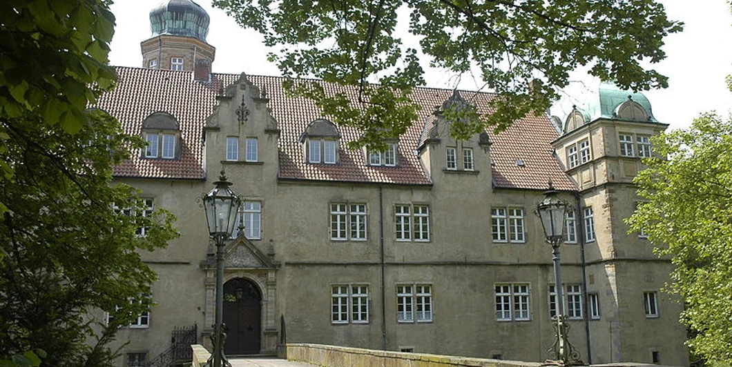 Wasserschloss Ulenburg umgeben von Bäumen, mit Brücke zum Eingang und markanten Türmen.
