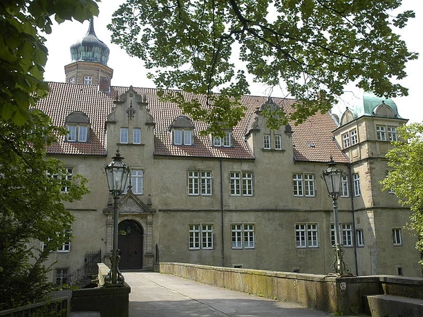 Wasserschloss Ulenburg umgeben von Bäumen, mit Brücke zum Eingang und markanten Türmen.