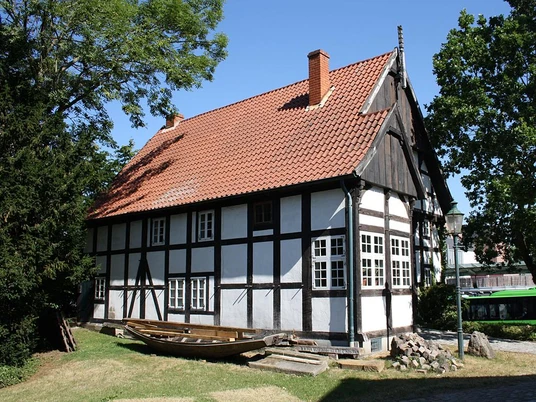 Museum Bünde Fachwerkhaus mit rotem Ziegeldach, umgeben von Bäumen im Freien, bei strahlend blauem Himmel.