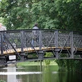 Herthabrücke Fußgängerbrücke mit schmiedeeisernem Geländer, umgeben von üppigem Grün, überquert einen Fluss.