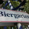 Schild mit der Aufschrift "Biergarten", umgeben von Bändern und Bäumen im Hintergrund.