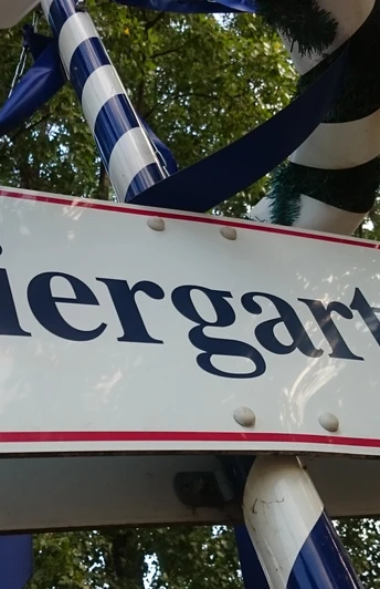 Schild mit der Aufschrift "Biergarten", umgeben von Bändern und Bäumen im Hintergrund.