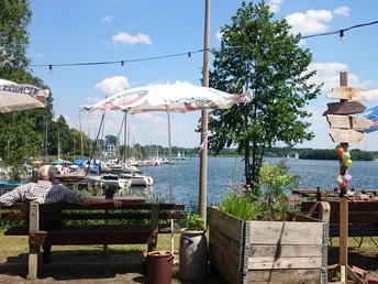 Bistro Seemöwe Ufercafé am See mit Blick auf Segelboote und Schirme, Besucher auf Parkbänken, freundliche Atmosphäre.