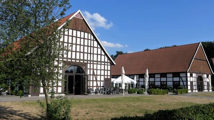 Gut Lippesee Ein Fachwerkgebäude mit roten Ziegeldächern und Terrasse, im Vordergrund Bäume und Rasenfläche.