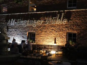 Die Alt-Enginger Mühle beleuchtet, mit Besuchern im stimmungsvollen Außenbereich am Abend.