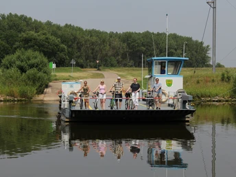 Menschen auf einer kleinen, über einen Fluss fahrenden Fähre mit Fahrrädern, umgeben von Natur.People on a small ferry crossing a river on bicycles, surrounded by nature.Mennesker på en lille færge, der kører over en flod på cykler, omgivet af natur.Mensen op een kleine veerboot die op de fiets een rivier oversteken, midden in de natuur.