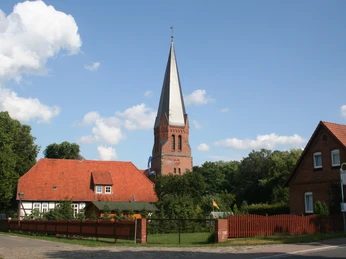 Kirche Magelsen Spitze Turm der Kirche Magelsen erhebt sich über Backsteinhäuser und grünen Bäumen an einem sonnigen Tag.The spire of Magelsen church rises above brick houses and green trees on a sunny day.Magelsens kirkespir hæver sig over murstenshuse og grønne træer på en solrig dag.De torenspits van de kerk van Magelsen steekt op een zonnige dag boven de bakstenen huizen en groene bomen uit.