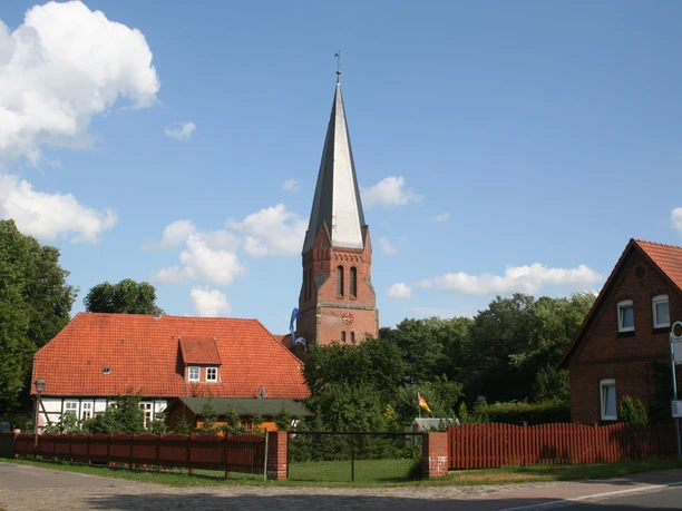 Kirche Magelsen The spire of Magelsen church rises above brick houses and green trees on a sunny day.