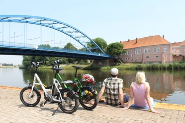 Grafenschloss zu Hoya Ein Paar sitzt entspannt am Wasser, mit Blick auf das historische Grafenschloss zu Hoya und eine blaue Brücke.