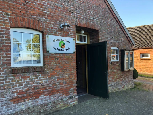 Kultur-Gulfhof Landkultur Freepsum Gulfhof von außen, Eingangstür, Schild "Musik am tiefsten Punkt" an der Mauer