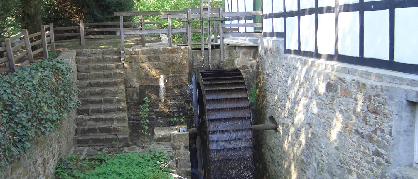 Gutswassermühle Hudenbeck Historische Wassermühle mit angrenzendem Fachwerkgebäude, umgeben von Natur und einem kleinen Bach.