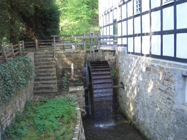 Gutswassermühle Hudenbeck Historische Wassermühle mit angrenzendem Fachwerkgebäude, umgeben von Natur und einem kleinen Bach.