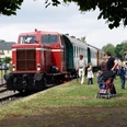 Eine historische Diesellok zieht einen nostalgischen Zug auf Gleisen an einer Gruppe Menschen vorbei.