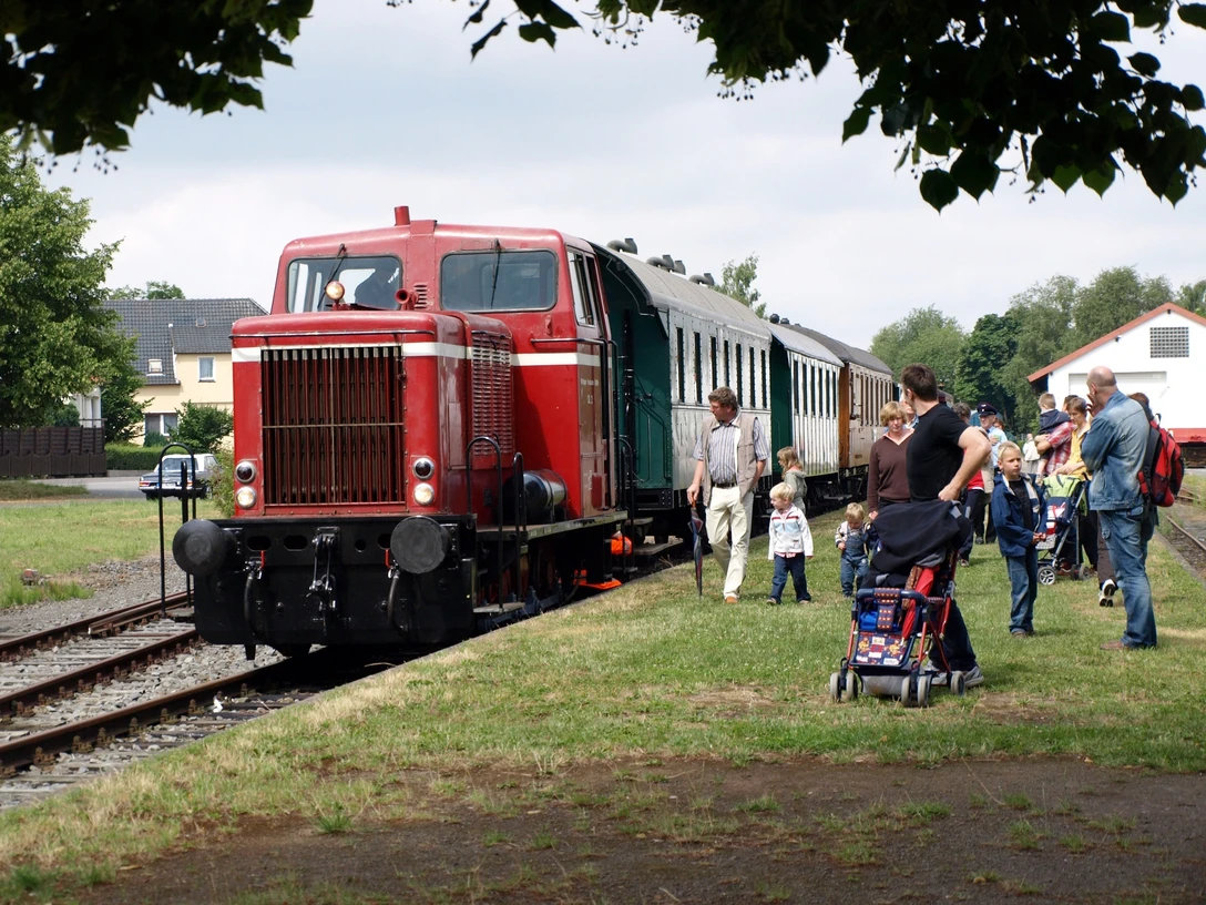 Museumseisenbahn Minden Eine historische Diesellok zieht einen nostalgischen Zug auf Gleisen an einer Gruppe Menschen vorbei.
