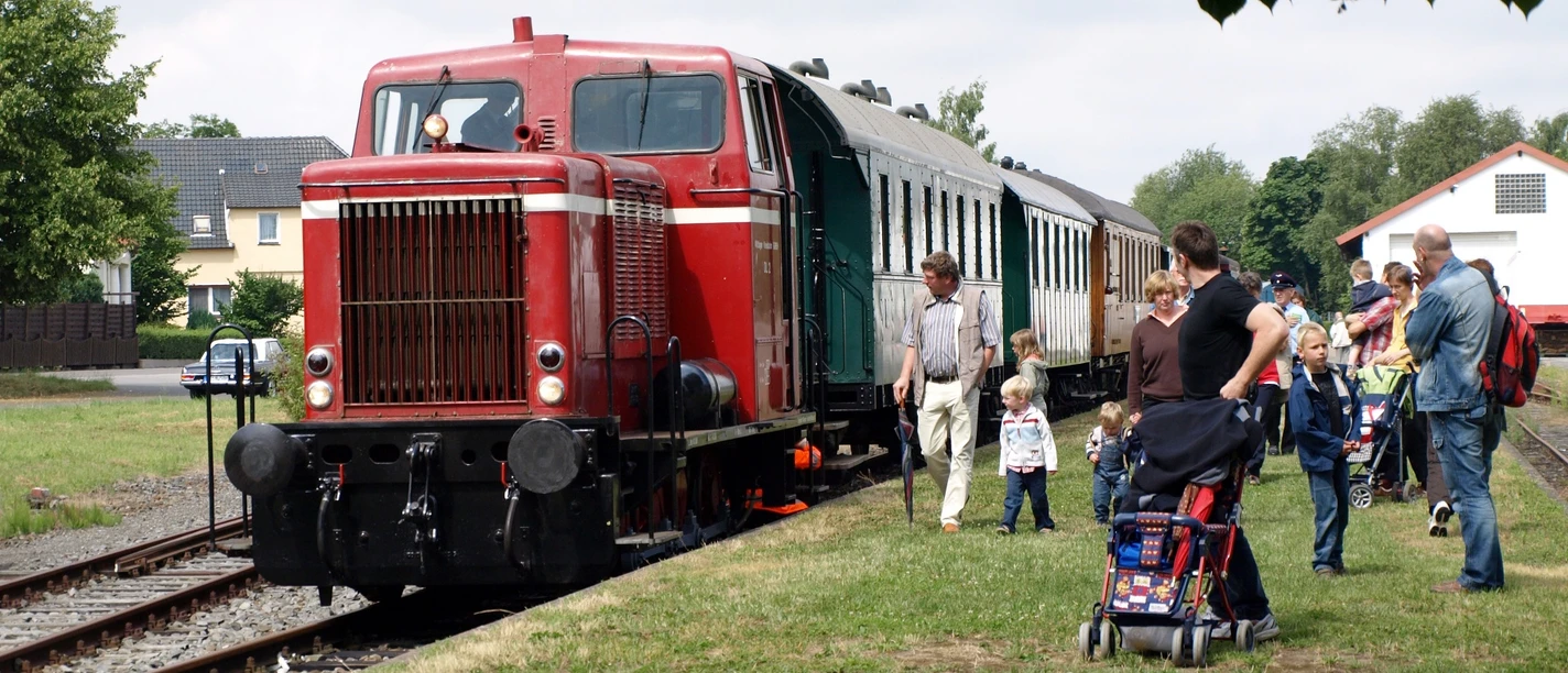 Museumseisenbahn Minden Eine historische Diesellok zieht einen nostalgischen Zug auf Gleisen an einer Gruppe Menschen vorbei.