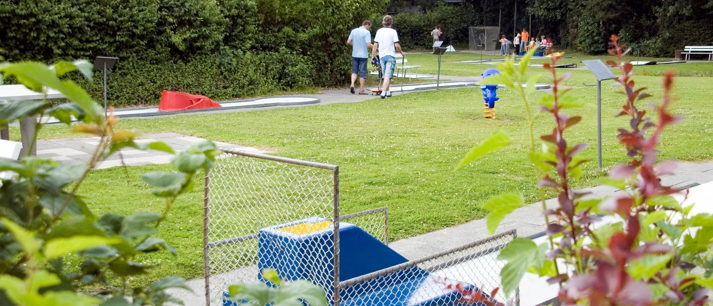 Minigolfplatz mit Rasenbahnen, Spielern und gemütlicher Gartenatmosphäre im Grünen umgeben.