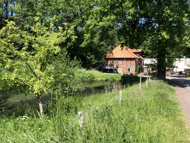 Klostermühle Heiligenberg Backsteinhaus mit rotem Dach, umgeben von üppigem Grün und einem Teich, an einem sonnigen Tag.