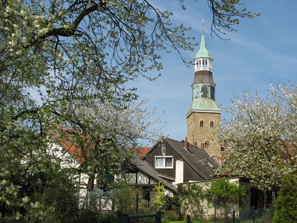 St. Sylvesterkirche.jpg Blühende Bäume umrahmen einen rustikalen Kirchturm mit rot gedeckten Häusern im Hintergrund.