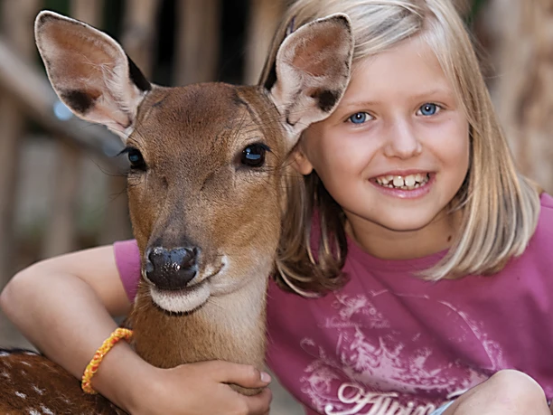 Girl cuddling with a deer in Görlitz Zoo, both look happily into the camera.