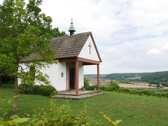 Die Heimkehrerkapelle Istrup steht auf einer grünen Wiese mit Blick auf das hügelige Umland.