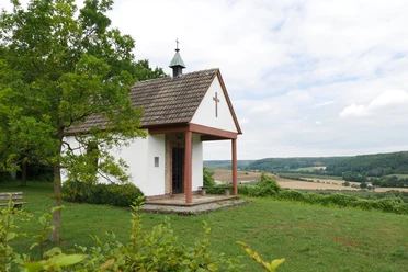 Heimkehrerkapelle Istrup Die Heimkehrerkapelle Istrup steht auf einer grünen Wiese mit Blick auf das hügelige Umland.