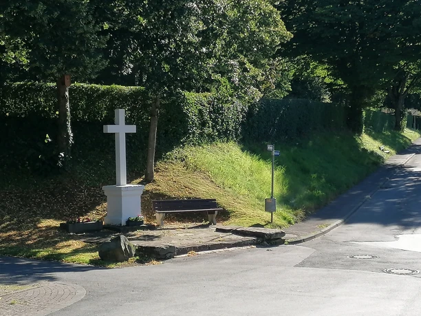 Bartholomäus Kreuz Istrup Steinernes Kreuz mit Bank an einer von Bäumen gesäumten Straße, umgeben von grüner Natur.