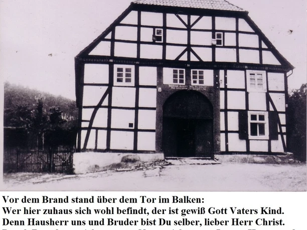Fachwerk-Pfarrhaus im Schwarz-Weiß-Foto, mit großem Torbogen und Inschrift über dem Eingang.