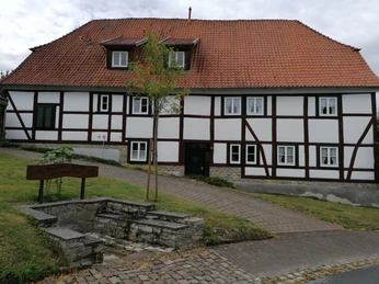 Pfarrheim mit Pastors Plump Fachwerkgebäude mit rotem Ziegeldach, zentral gelegene Eingangstür, umgeben von kleinem Garten.