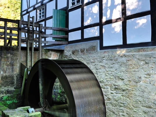 Gutswassermühle Hudenbeck Historische Wassermühle Hudenbeck mit beeindruckendem Fachwerk und rotierendem Wasserrad im Grünen.