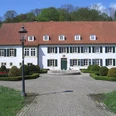 Haus des Gastes Bad Holzhausen Historisches Gebäude mit rotem Ziegeldach, umgeben von gepflegten Gärten und Kopfsteinpflasterweg.
