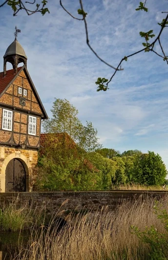 Gut Stockhausen Historisches Gut mit Fachwerkgebäude und Turm, umgeben von Natur, unter einem blauen Himmel.