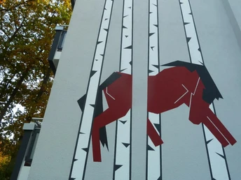 "Der Blaue Reiter" - Schweriner Straße Wandbild eines stilisierten roten Pferdes zwischen stilisierten Birkenstämmen auf einer Hausfassade.