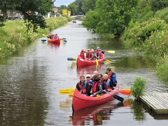 Paddler auf dem Augustfehn Kanal Mehrere Gruppen von Paddlern in roten Kanus gleiten fröhlich auf einem grünen Kanal entlang.