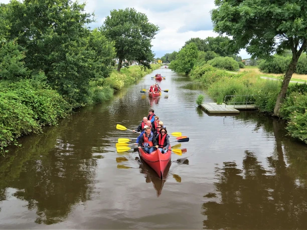 Paddler auf dem Augustfehn Kanal Mehrere rote Kanus gleiten ruhig durch den Augustfehn Kanal, gesäumt von üppigem Grün.