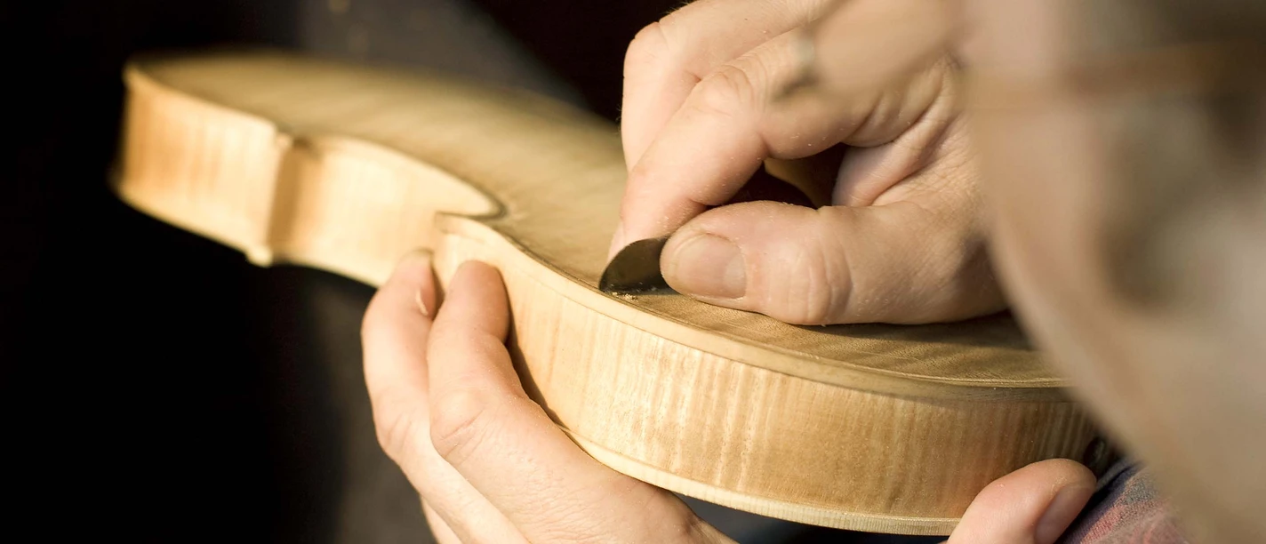A violin maker works the wood of a violin with precision and craftsmanship.