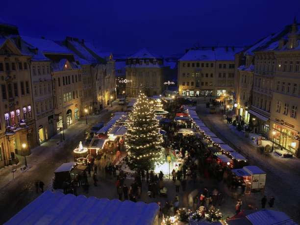 Zittau Christmas market at night, illuminated Christmas tree surrounded by stalls and visitors.