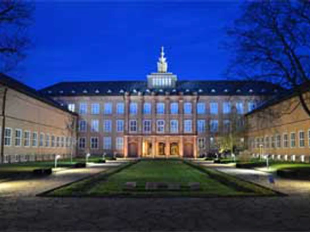 Museen im GRASSI Beleuchteter Museumskomplex mit symmetrischer Fassade, nachts von Bäumen umgeben.