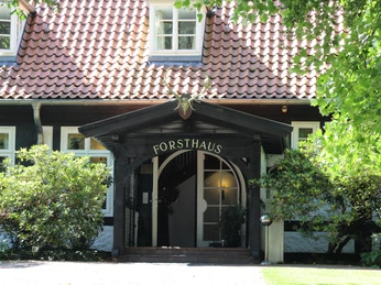 Entrance to a traditional forester's lodge with red roof and deer antlers above the entrance gate.