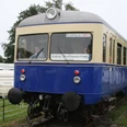 Kaffkieker Ein blauer nostalgischer Zug auf Gleisen, umgeben von grüner Landschaft und einem Wohnwagen.
