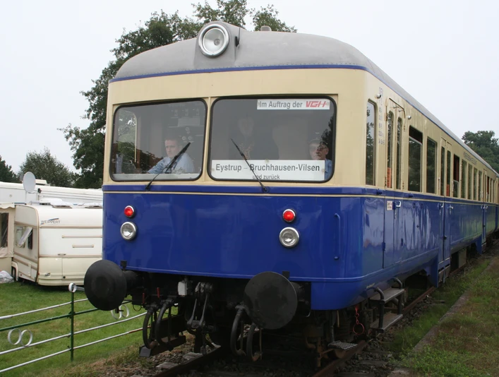 Kaffkieker Ein blauer nostalgischer Zug auf Gleisen, umgeben von grüner Landschaft und einem Wohnwagen.