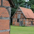 Schafstallviertel Hülsen Zwei historische Fachwerkgebäude mit Backsteinwänden stehen auf einer grünen Wiese vor Bäumen.