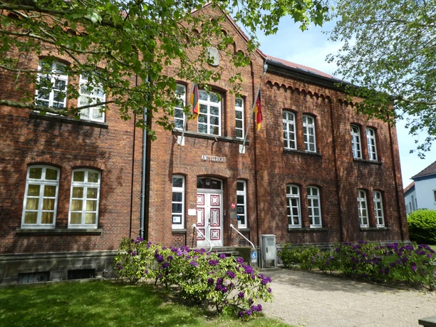 Backsteinbau des Amtsgerichts Achim mit symmetrischen Fenstern und bunten Blumen im Vordergrund.