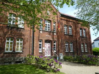 Amtsgericht Achim Backsteinbau des Amtsgerichts Achim mit symmetrischen Fenstern und bunten Blumen im Vordergrund.
