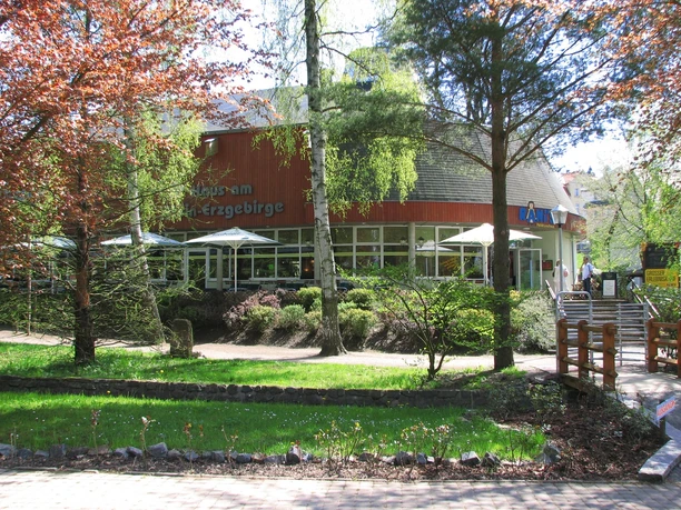 image Restaurant mit großer Terrasse und Sonnenschirmen, umgeben von hohen Bäumen und gepflegtem Rasen.