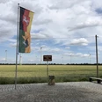 Geografischer Mittelpunkt Niedersachsens (16).jpg Vor einem windkraftbestückten Getreidefeld weht die Flagge Niedersachsens neben einem Wegweiser.