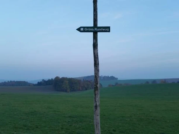 Signpost to the Grünberger Rundweg in front of a green field with a wooded background.