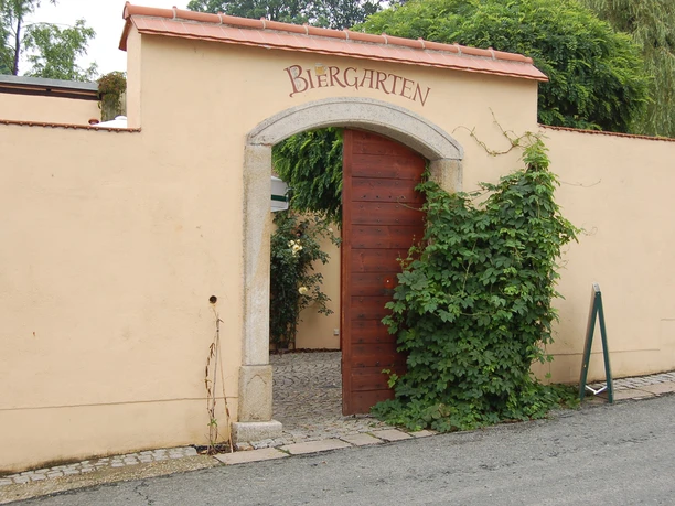 Entrance to a beer garden with open wooden door and ivy-covered wall.