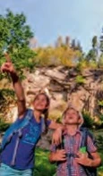 image Zwei fröhliche Wanderer mit Rucksäcken zeigen auf einen sonnigen Felsen im Wald.Two cheerful hikers with rucksacks point to a sunny rock in the forest.Dva veselí turisté s batohy ukazují na slunečnou skálu v lese.Dwóch wesołych wędrowców z plecakami wskazuje słoneczną skałę w lesie.Twee vrolijke wandelaars met rugzakken wijzen naar een zonnige rots in het bos.Due allegri escursionisti con zaino in spalla indicano una roccia soleggiata nel bosco.